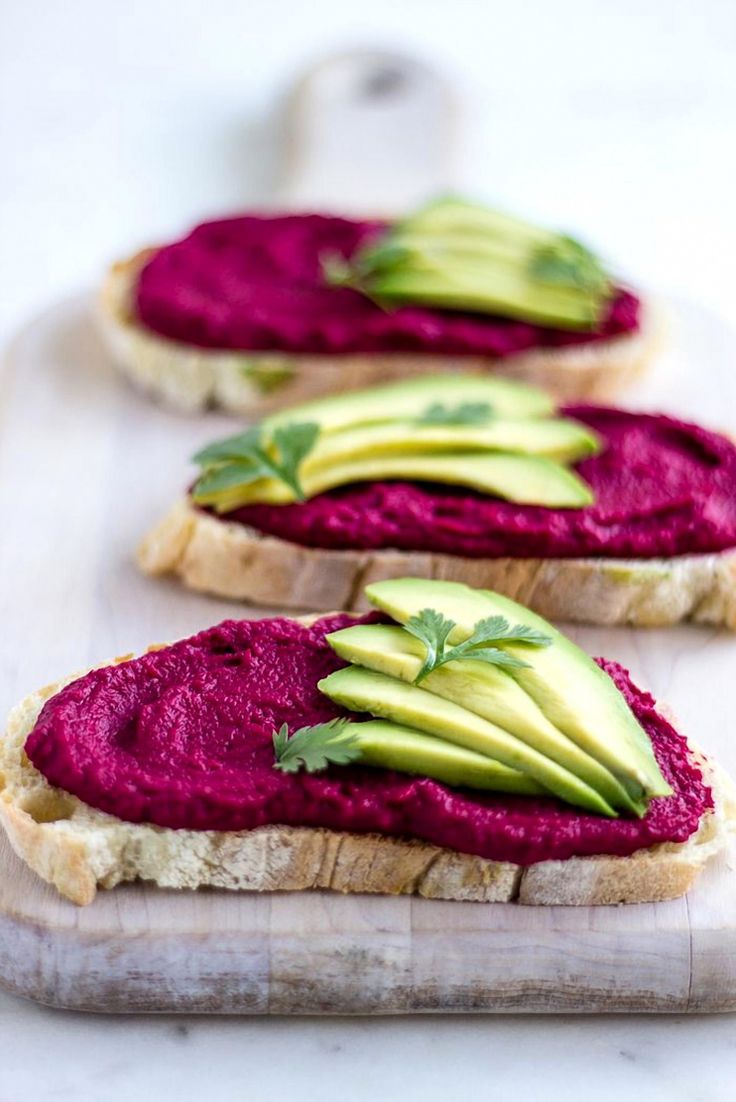 Slices of crusty bread topped with beet hummus and fanned avocado.