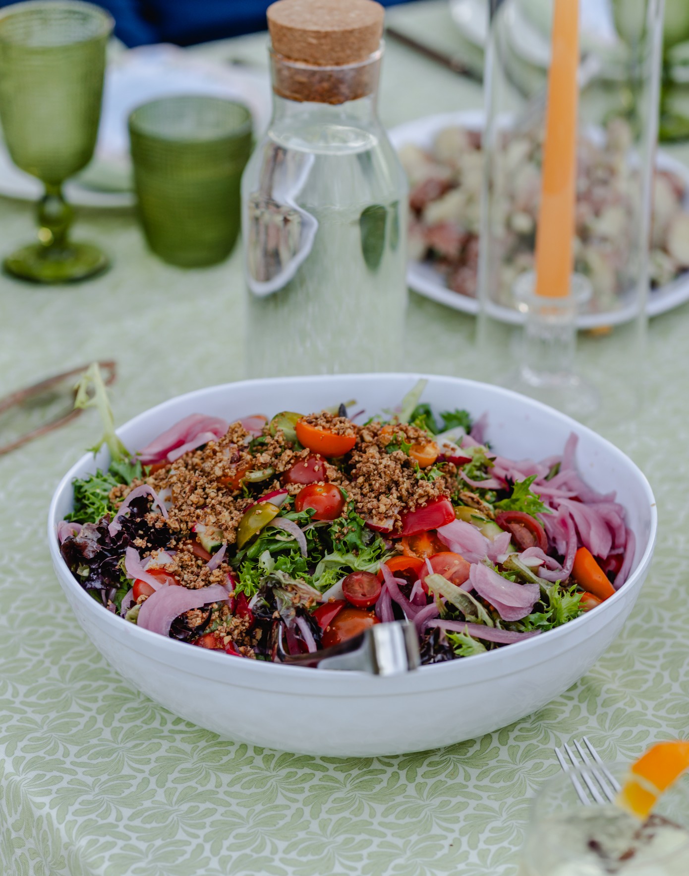 A garden salad with pickled onions, cherry tomatoes, and toasted crumble on an outdoor table.